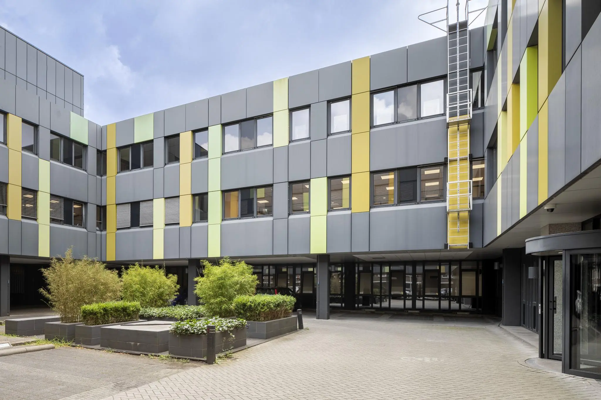 Binnenplein van een modern kantoorgebouw aan de Van Boshuizenstraat met grijsgevels en verticale gele en groene accenten.